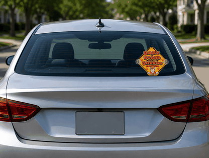 Bright yellow 10x10 inch Sheroo™ Baby on Board sign with Brave Little Tiger design attached to car window with suction cups